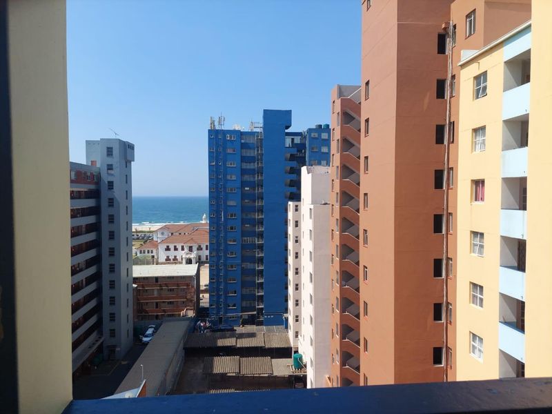 An elevated urban view from a balcony overlooking surrounding apartment buildings with a glimpse of the ocean in the distance.
