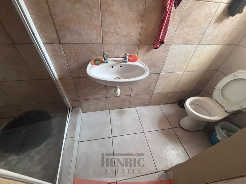 A functional bathroom featuring a wall-mounted basin, shower enclosure, and toilet with neutral ceramic tiling throughout.
