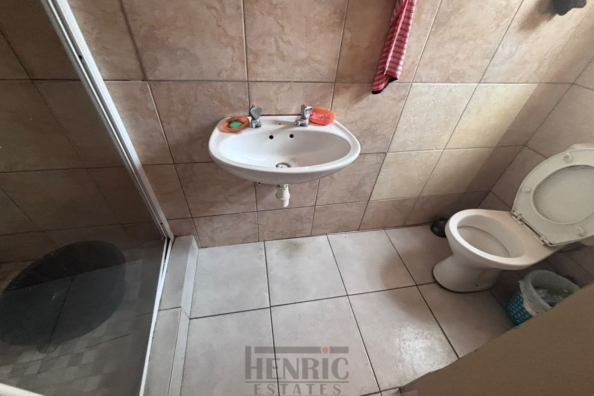 A functional bathroom featuring a wall-mounted basin, shower enclosure, and toilet with neutral ceramic tiling throughout.