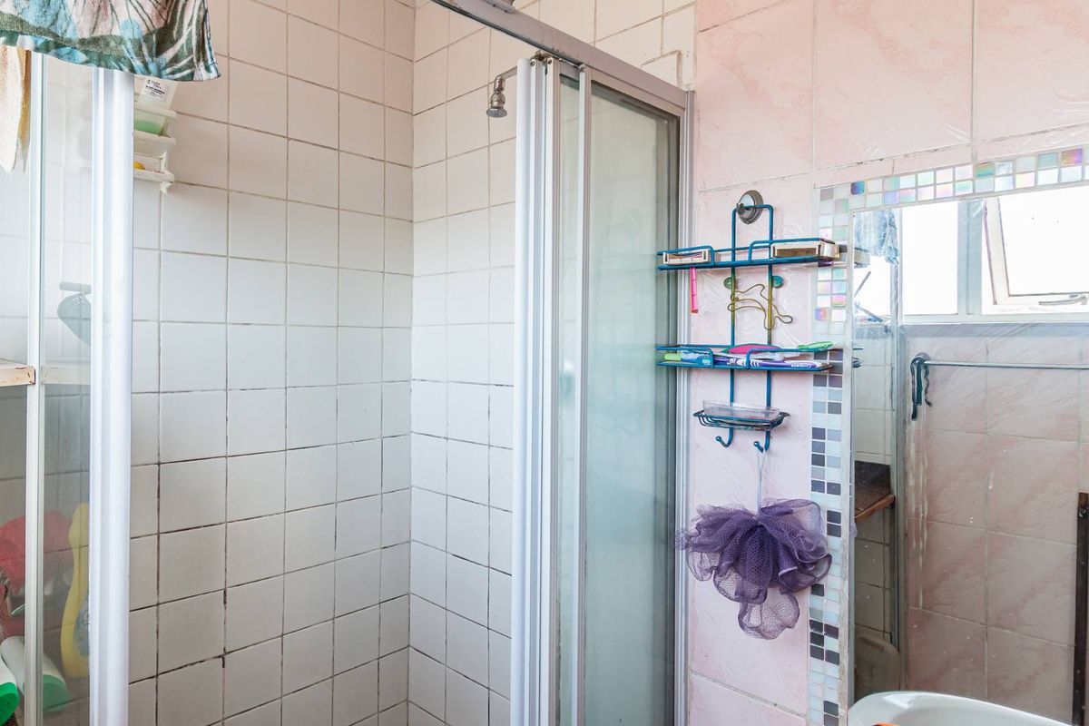 A dated bathroom featuring a shower enclosure with white wall tiles and pink decorative wall tiling.