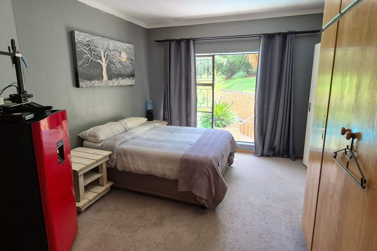 A bedroom featuring built-in wooden cupboards, carpeted flooring, and a large window providing natural light and garden views.