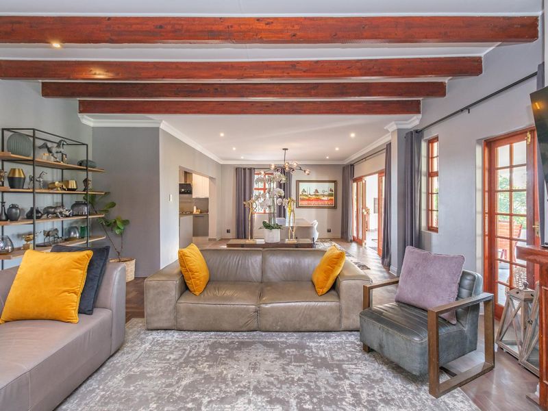 Spacious open-plan living area featuring exposed timber ceiling beams, hardwood flooring, and a fireplace, seamlessly connecting to the dining space and kitchen.