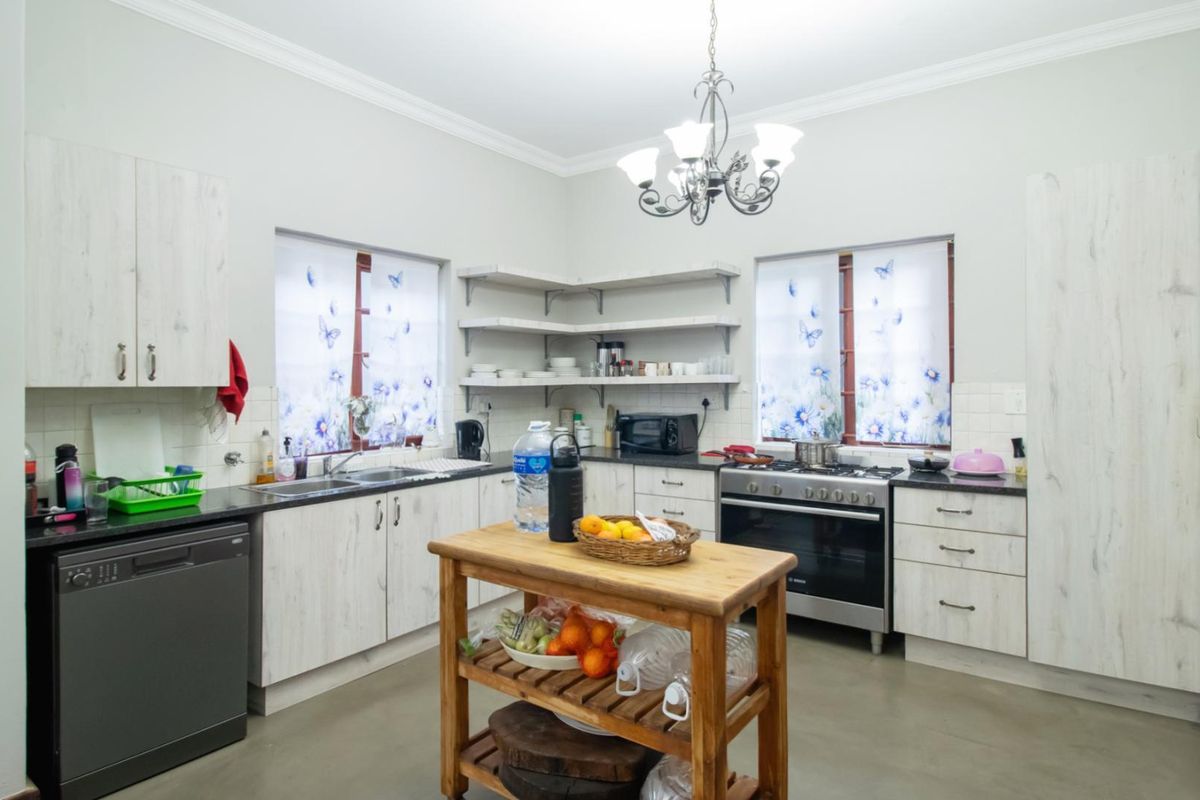 A functional kitchen featuring light wood-grain cabinetry, dark countertops, open shelving, and a gas stove, complemented by a decorative chandelier.