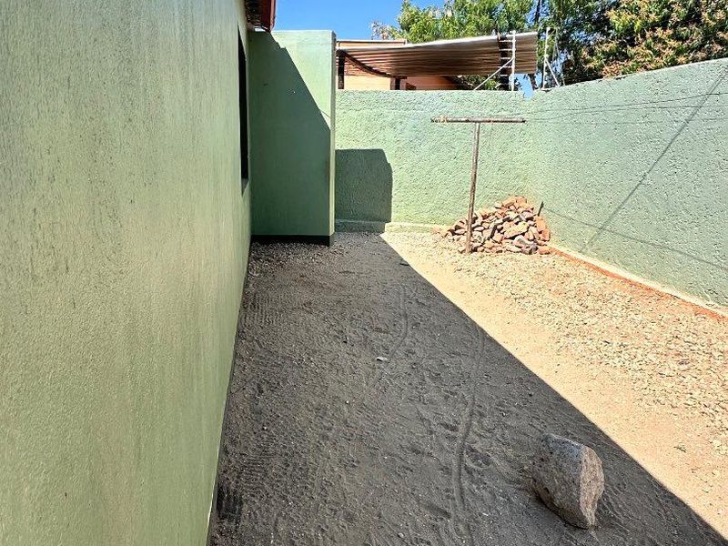 A side or rear exterior area featuring a boundary wall, gravel ground surface, and a fixed clothesline.