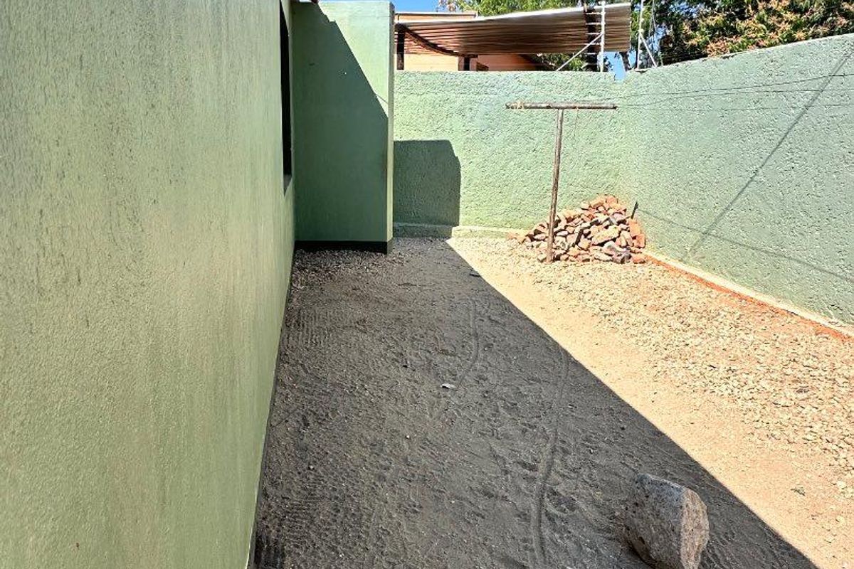 A side or rear exterior area featuring a boundary wall, gravel ground surface, and a fixed clothesline.