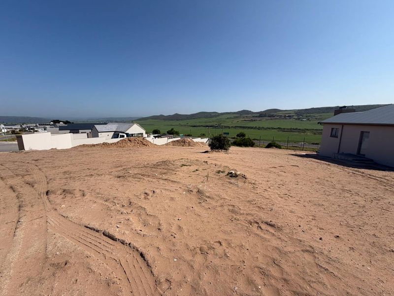 A vacant residential plot featuring sandy terrain, boundary walls, and expansive views of the surrounding landscape.