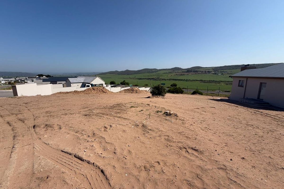 A vacant residential plot featuring sandy terrain, boundary walls, and expansive views of the surrounding landscape.