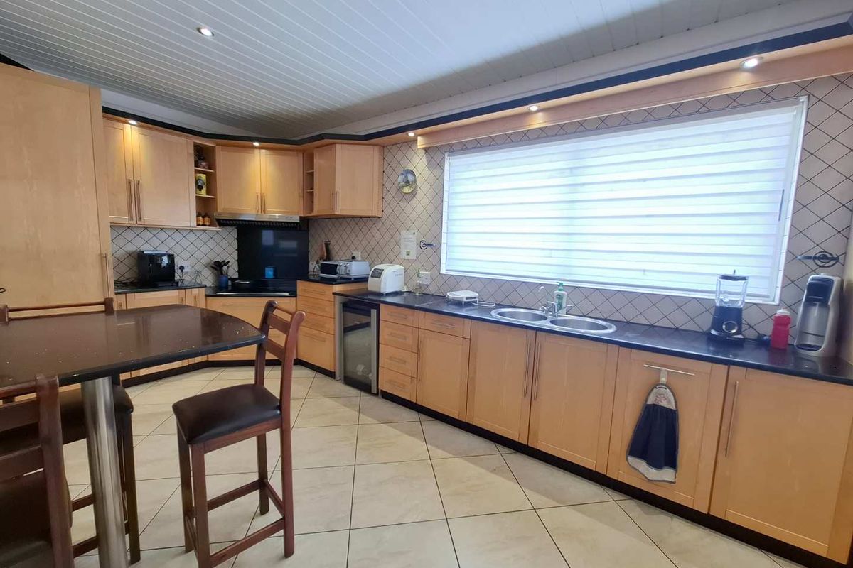 A functional kitchen featuring light wood cabinetry, dark countertops, a double basin sink, and tiled flooring with integrated recessed lighting.