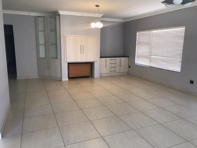 Spacious living area featuring neutral tiled flooring, built-in storage cabinetry, crown molding, and large windows with fitted venetian blinds.