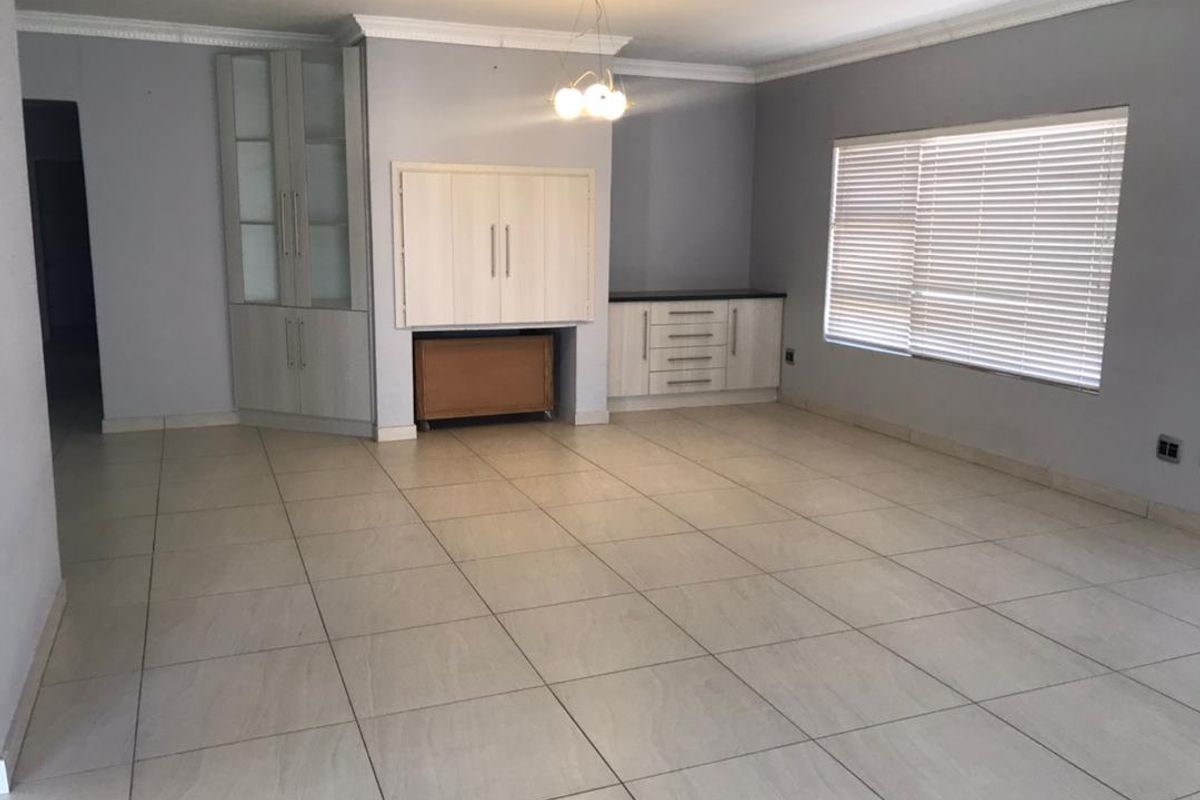 Spacious living area featuring neutral tiled flooring, built-in storage cabinetry, crown molding, and large windows with fitted venetian blinds.