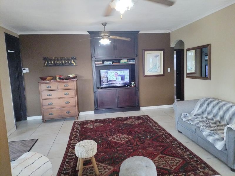 A living room featuring tiled flooring, a ceiling fan, and a dark wood built-in entertainment unit.