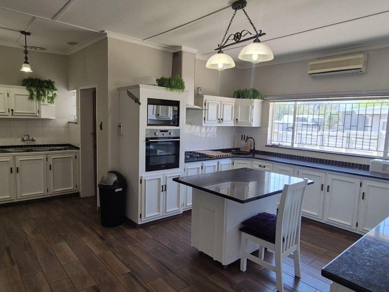Spacious kitchen featuring white cabinetry, dark granite countertops, a central island, built-in appliances, and wood-look flooring with ample natural light.