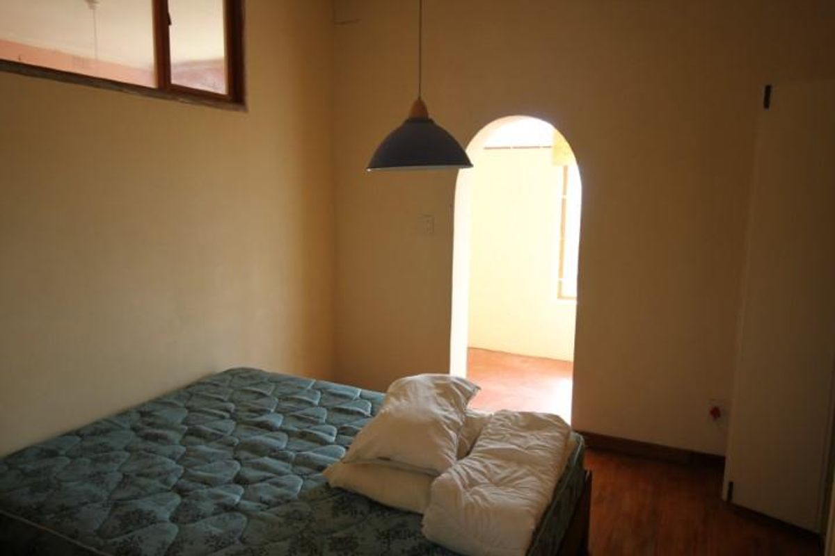 A bedroom featuring an arched doorway, wooden flooring, and a high-level window, providing a simple and functional living space.