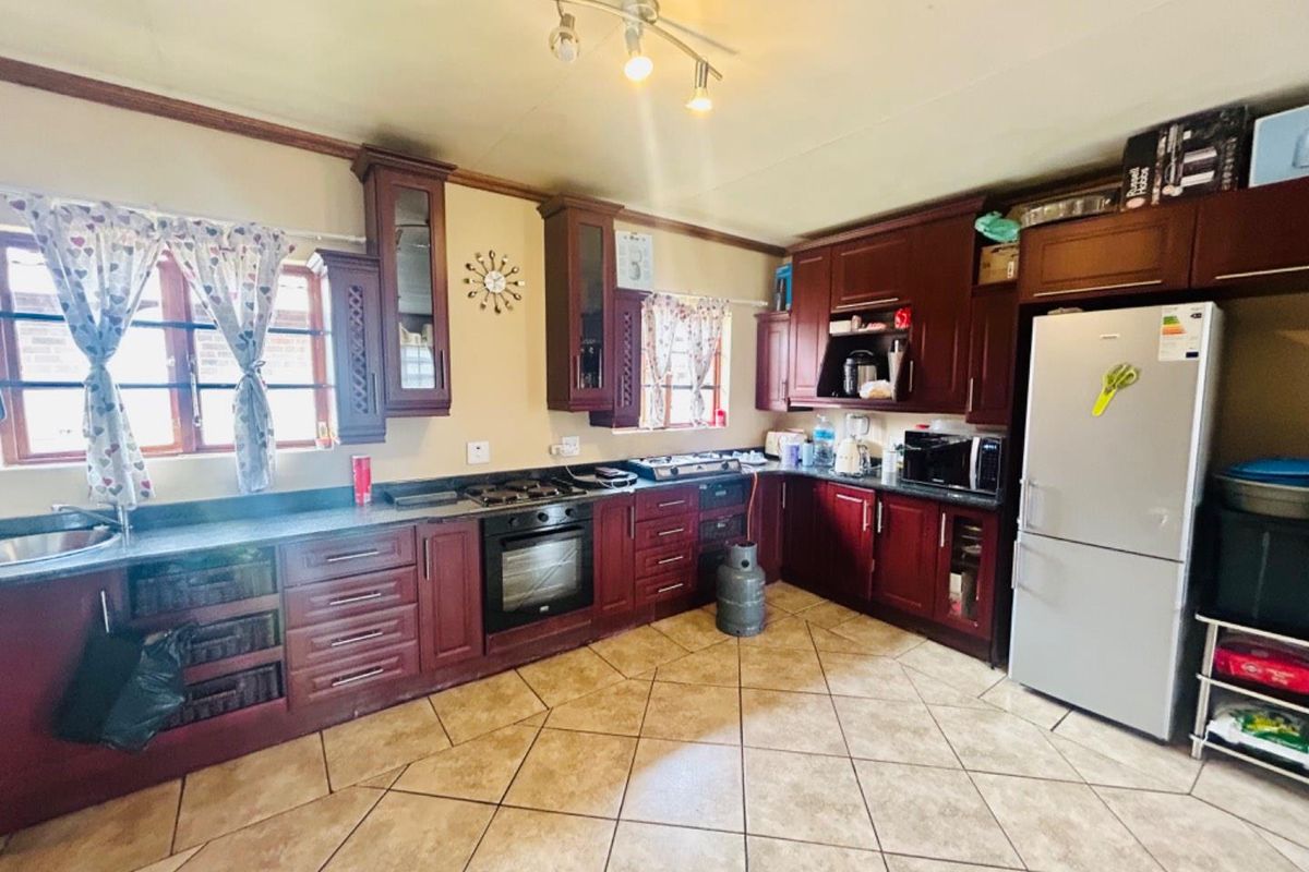 A functional kitchen featuring dark wood cabinetry, integrated oven and hob, tiled flooring, and ample counter space for meal preparation.