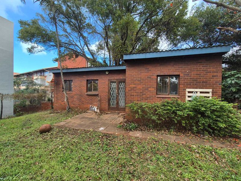 Rear view of a face brick house featuring a small paved patio area, security gates, and established garden surroundings.