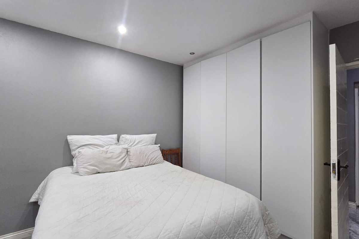 A bedroom featuring grey walls, recessed downlighting, and a large white built-in wardrobe providing ample storage space.