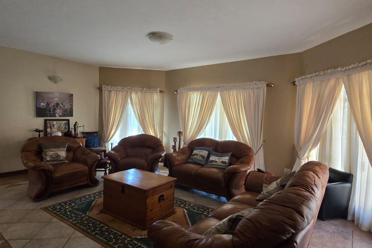 A spacious living room featuring tiled flooring, large windows with curtains, and an arched entryway leading to an adjacent room.