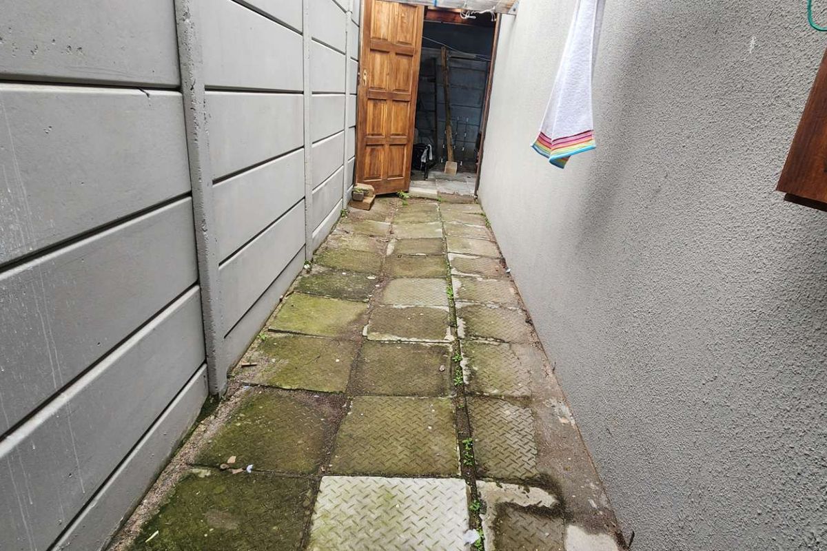 A narrow exterior side passage featuring a precast concrete boundary wall and paved walkway with visible signs of weathering and moss accumulation.