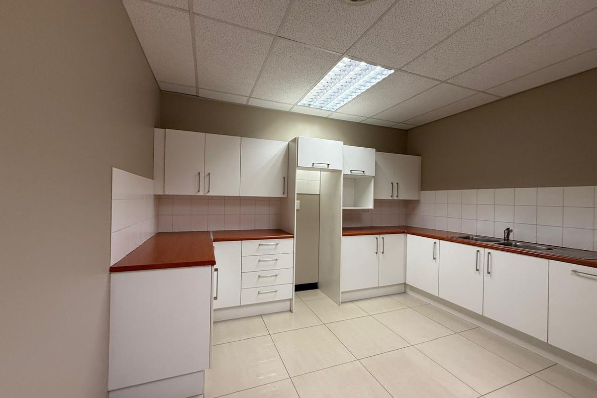 A functional office kitchenette featuring white cabinetry, laminate countertops, a stainless steel sink, and tiled flooring with recessed ceiling lighting.
