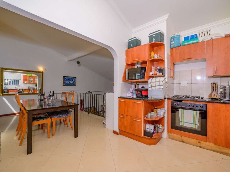 Open-plan kitchen and dining area featuring tiled flooring, wooden cabinetry, built-in oven, gas hob, and a decorative wrought iron balustrade overlooking the lower level.