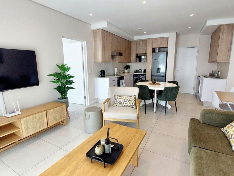 Modern open-plan living area featuring a contemporary kitchen with wood-finish cabinetry, integrated appliances, and sleek tiled flooring throughout the combined space.
