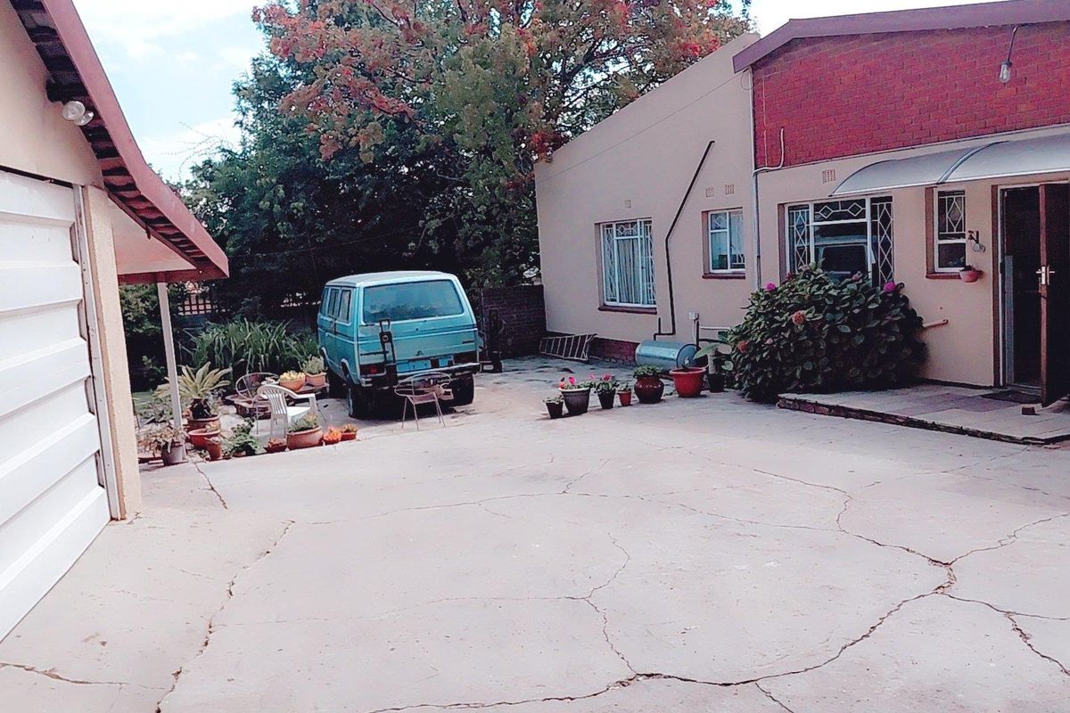 Rear exterior view of the property featuring a large concrete driveway, brick wall sections, and security window bars.