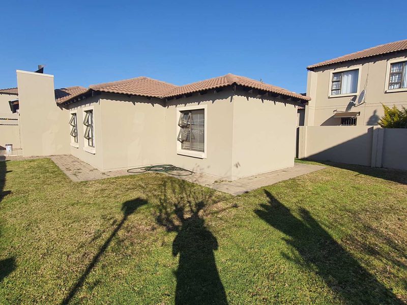 Rear view of the townhouse featuring a private garden, paved walkway, and tiled roof structure.