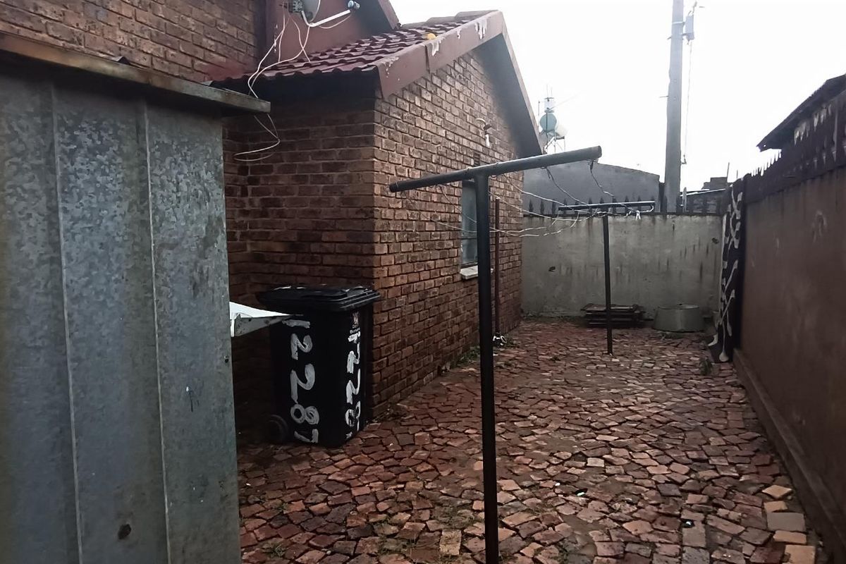 A side exterior area featuring brick wall construction, paved ground surface, and perimeter boundary walls.