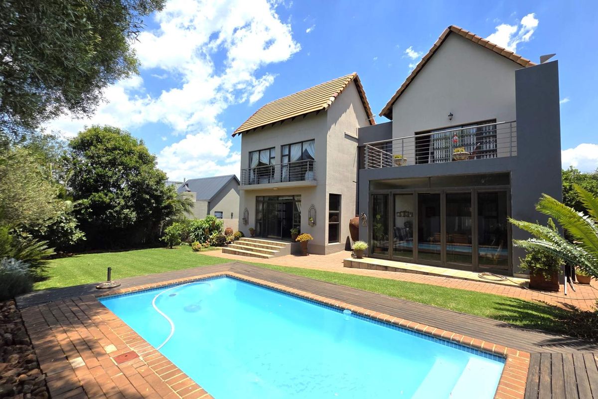 Rear view of a two-story house featuring a swimming pool, landscaped garden, paved patio area, and upper-level balconies.