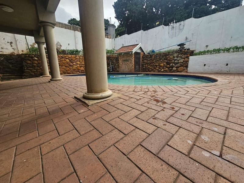 Outdoor pool area featuring a paved patio, stone retaining walls, and concrete columns, requiring maintenance on perimeter walls and paving.