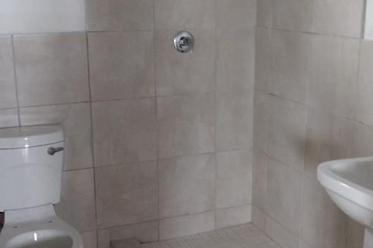 A functional bathroom featuring a tiled shower base, pedestal basin, and standard toilet, finished with neutral wall and floor tiles.