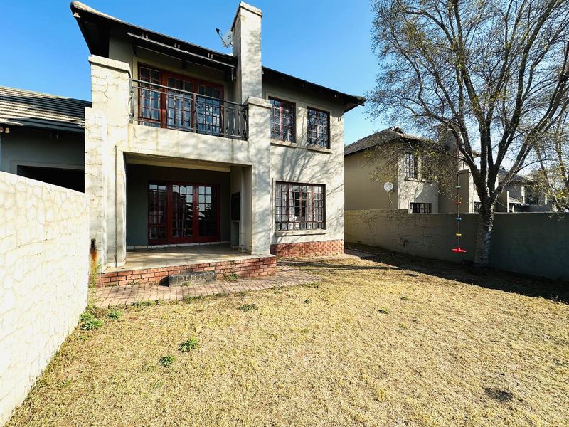 Rear view of a two-story townhouse featuring a covered patio, upper balcony, brick chimney, and a private garden area with boundary walls.