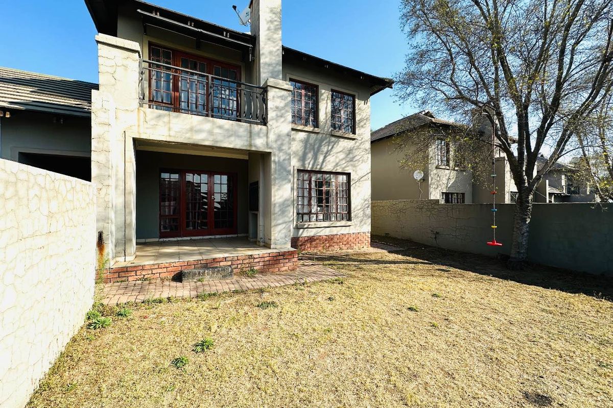 Rear view of a two-story townhouse featuring a covered patio, upper balcony, brick chimney, and a private garden area with boundary walls.