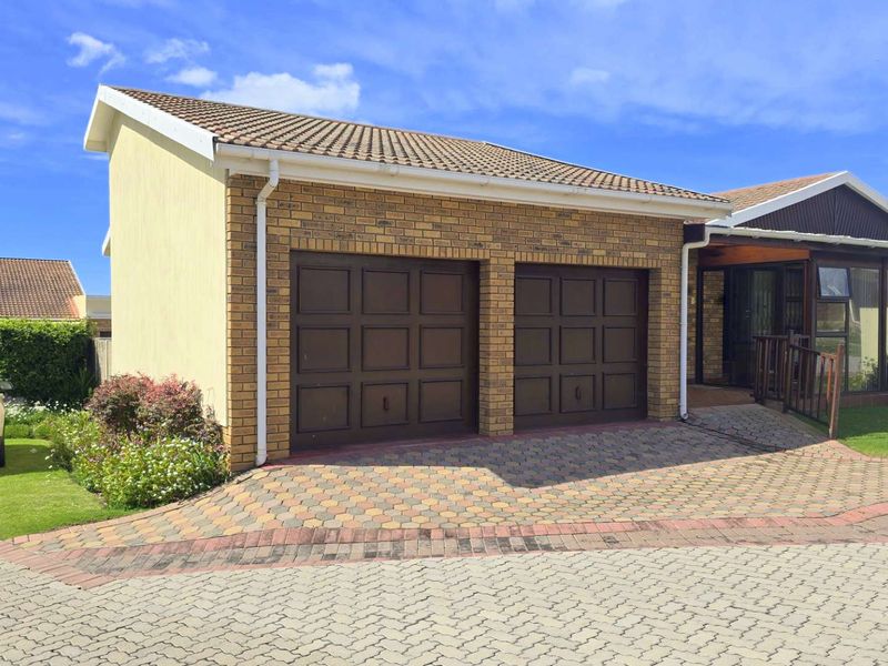 Front view of a retirement village residence featuring a double garage, brick exterior, tiled roof, and a paved driveway.
