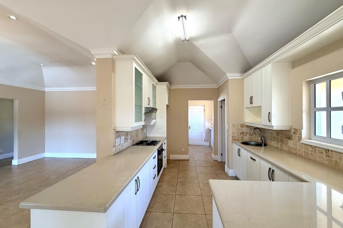 Spacious, empty kitchen featuring white cabinetry, stone countertops, built-in appliances, tiled flooring, and a vaulted ceiling with crown molding.