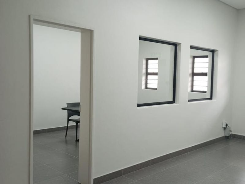A clean, minimalist office space featuring neutral tiled flooring, a suspended ceiling, and internal windows providing natural light between rooms.