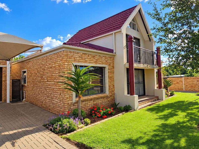 A well-maintained townhouse featuring a face brick facade, a tiled roof, a paved driveway with a shade sail, and a private balcony.
