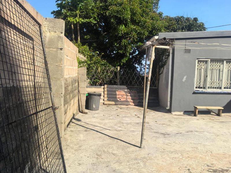 A rear exterior courtyard area featuring a concrete boundary wall, security window bars, and a paved surface.