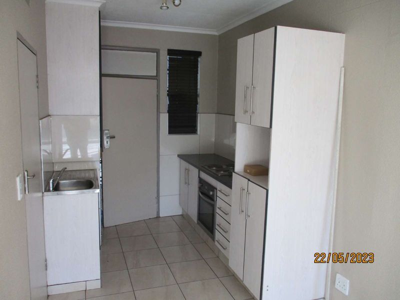 A compact kitchen featuring built-in cabinetry, a stainless steel sink, an integrated oven and hob, and tiled flooring.