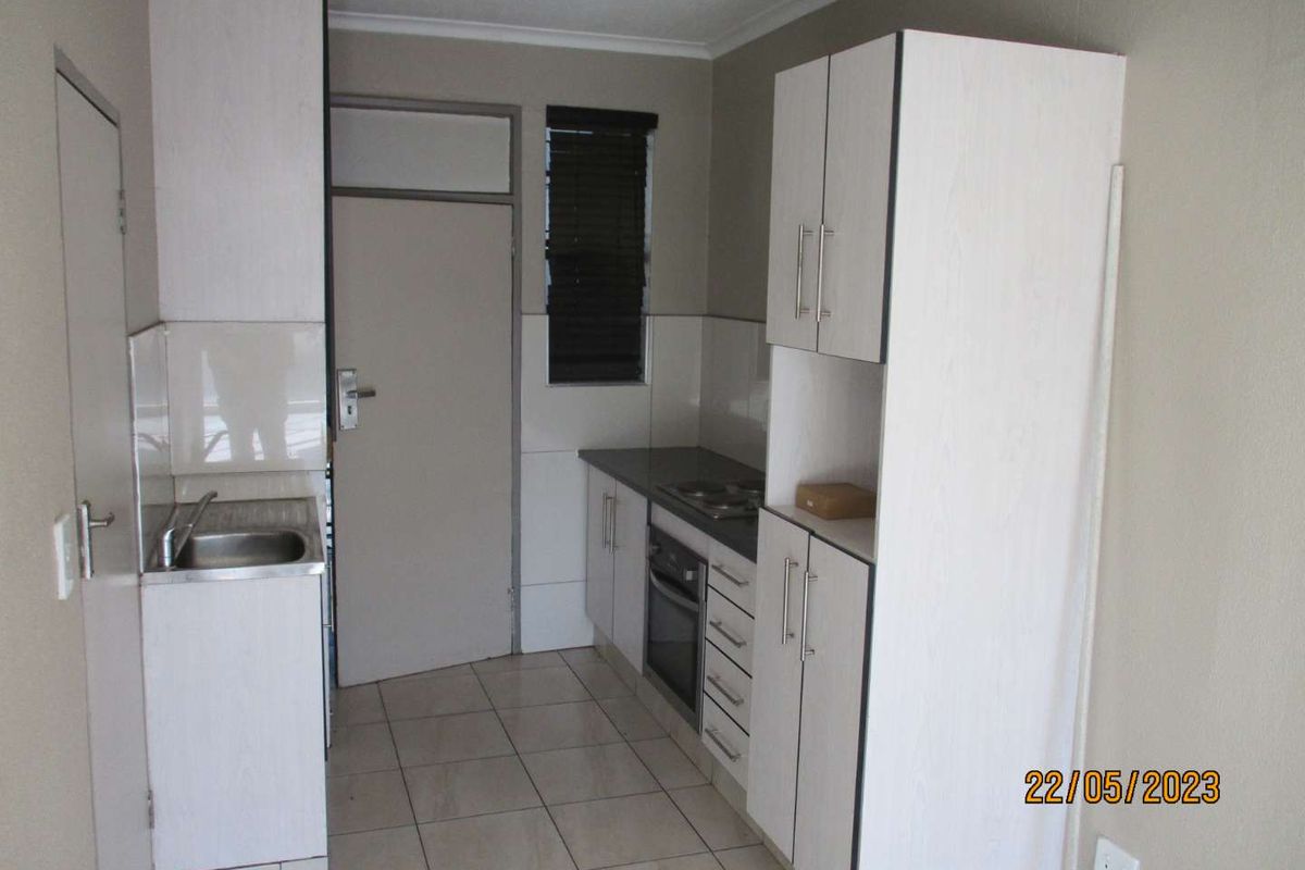 A compact kitchen featuring built-in cabinetry, a stainless steel sink, an integrated oven and hob, and tiled flooring.