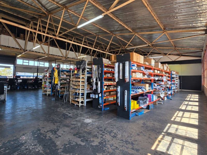 Spacious industrial warehouse area featuring exposed steel roof trusses, concrete flooring, and a mezzanine level, suitable for storage or workshop operations.