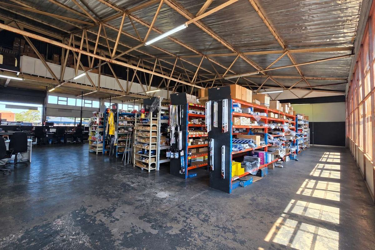 Spacious industrial warehouse area featuring exposed steel roof trusses, concrete flooring, and a mezzanine level, suitable for storage or workshop operations.
