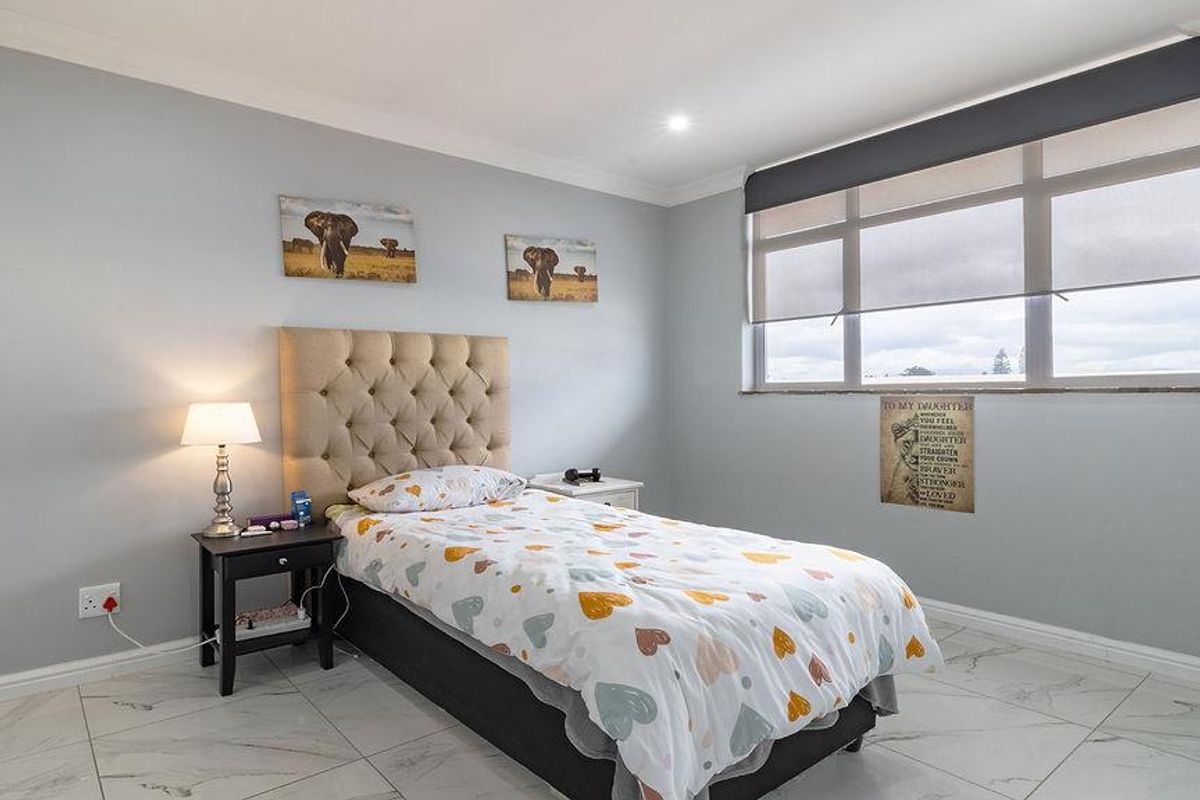 A bright bedroom featuring large windows with roller blinds, tiled flooring, and crown molding.