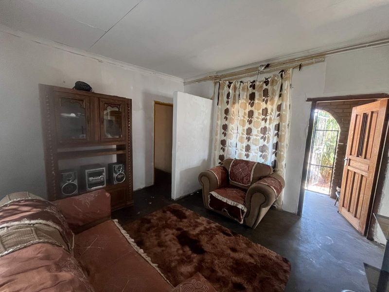 A living room area featuring exposed electrical wiring, a timber door, and a brick archway entrance, requiring significant cosmetic updates and repairs.