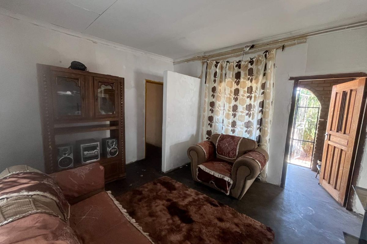A living room area featuring exposed electrical wiring, a timber door, and a brick archway entrance, requiring significant cosmetic updates and repairs.
