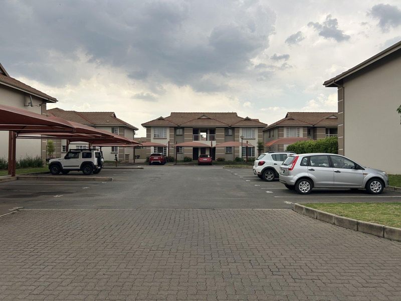 Exterior view of a townhouse complex featuring a paved parking area with covered carports and multi-unit residential buildings.