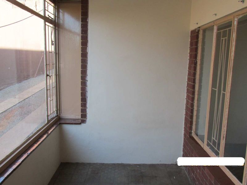 An enclosed balcony or sunroom featuring tiled flooring, brick detailing, and metal security bars on the windows.