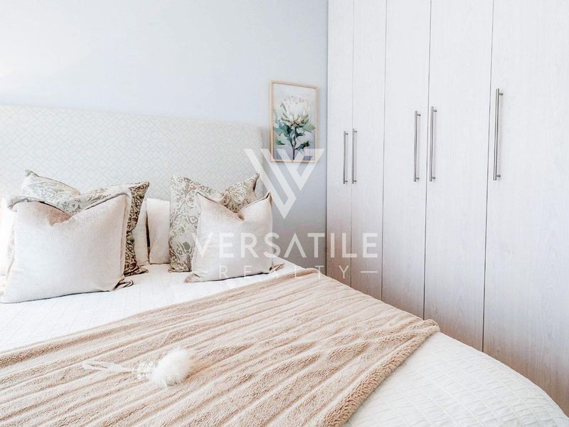 A well-maintained bedroom featuring neutral tones, a textured upholstered headboard, and ample built-in cupboard storage.