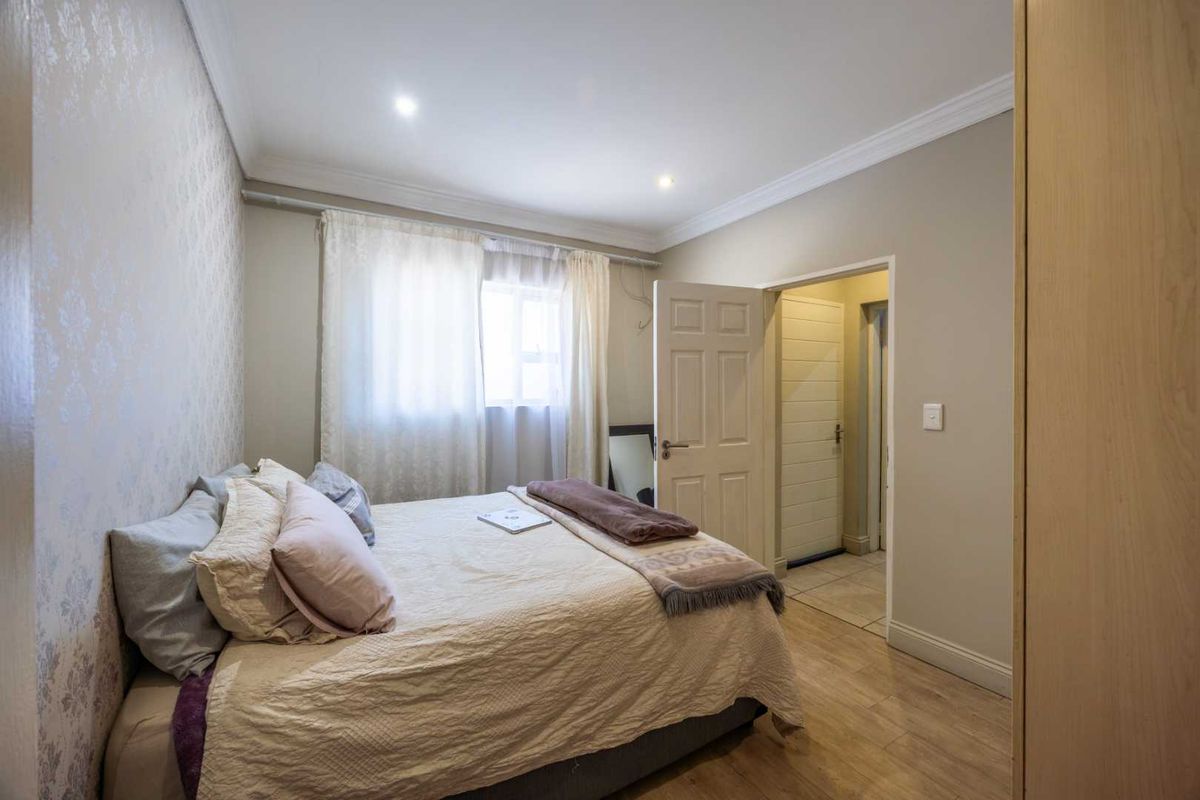 A well-maintained bedroom featuring laminate flooring, recessed downlighting, crown molding, and a built-in wardrobe, offering a clean and functional living space.