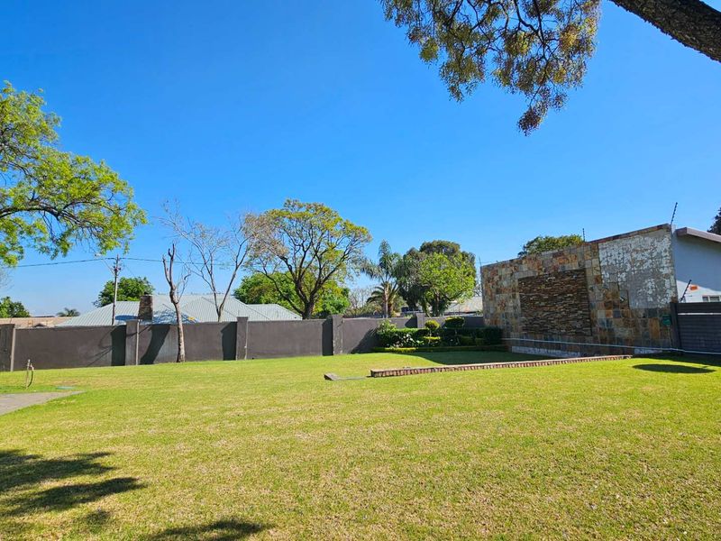 Spacious backyard featuring a well-maintained lawn, perimeter walling with electric fencing, and a decorative stone-clad feature wall.